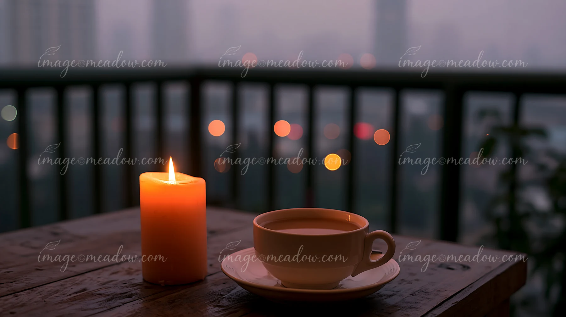A candle with copy space on right sits beside a cup of warm drink on a wooden table.