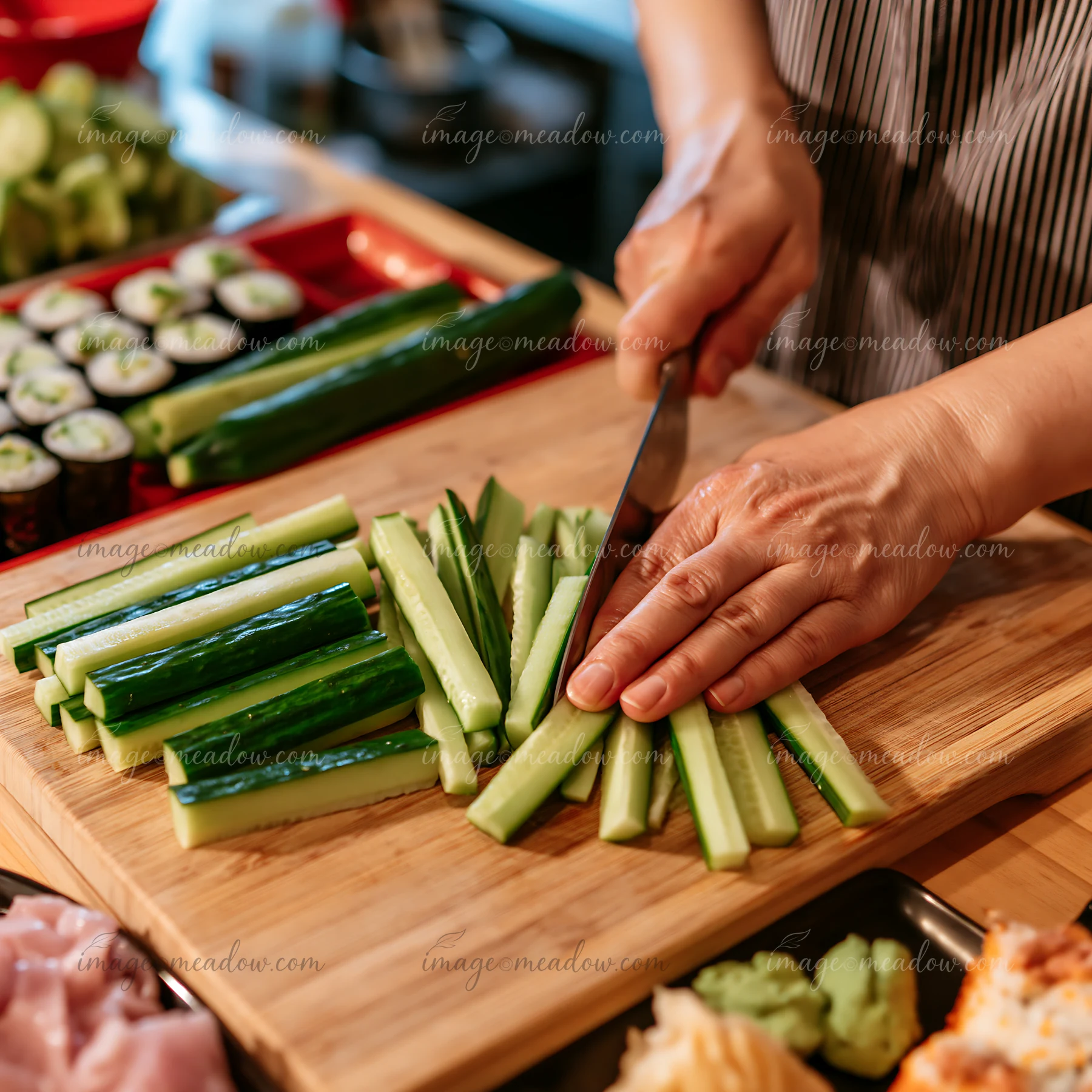 A chef prepares sushi at the restaurant counter by finely slicing cucumbers for sushi rolls.