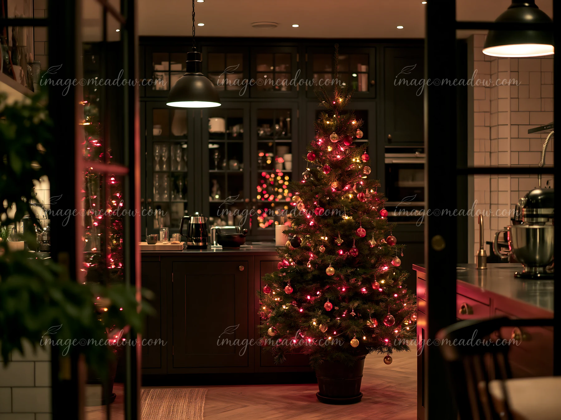A Christmas tree stands in a modern kitchen, decorated with lights and ornaments.