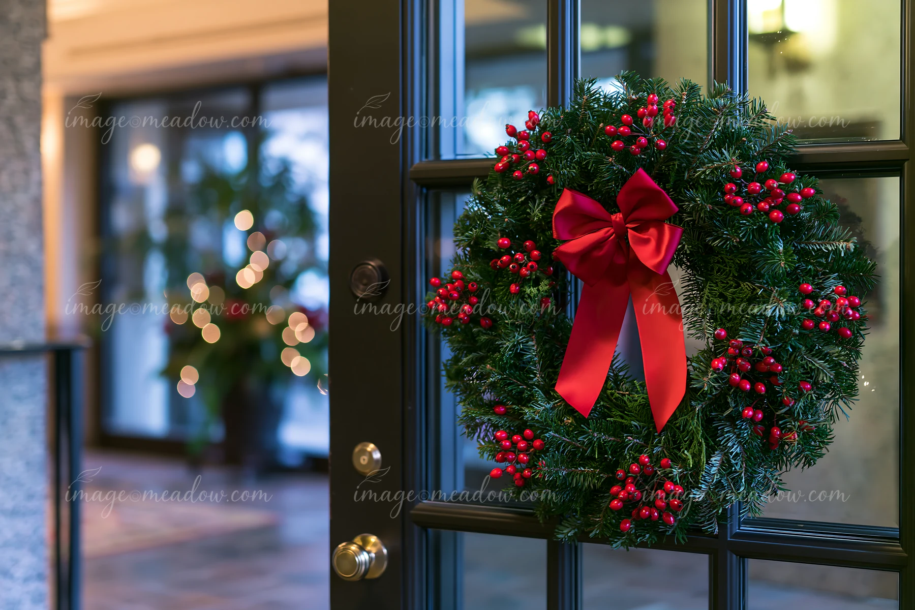 A Christmas wreath with red ribbon and berries hangs on an apartment door, while warm lights illuminate a cozy interior setting filled with holiday decorations.