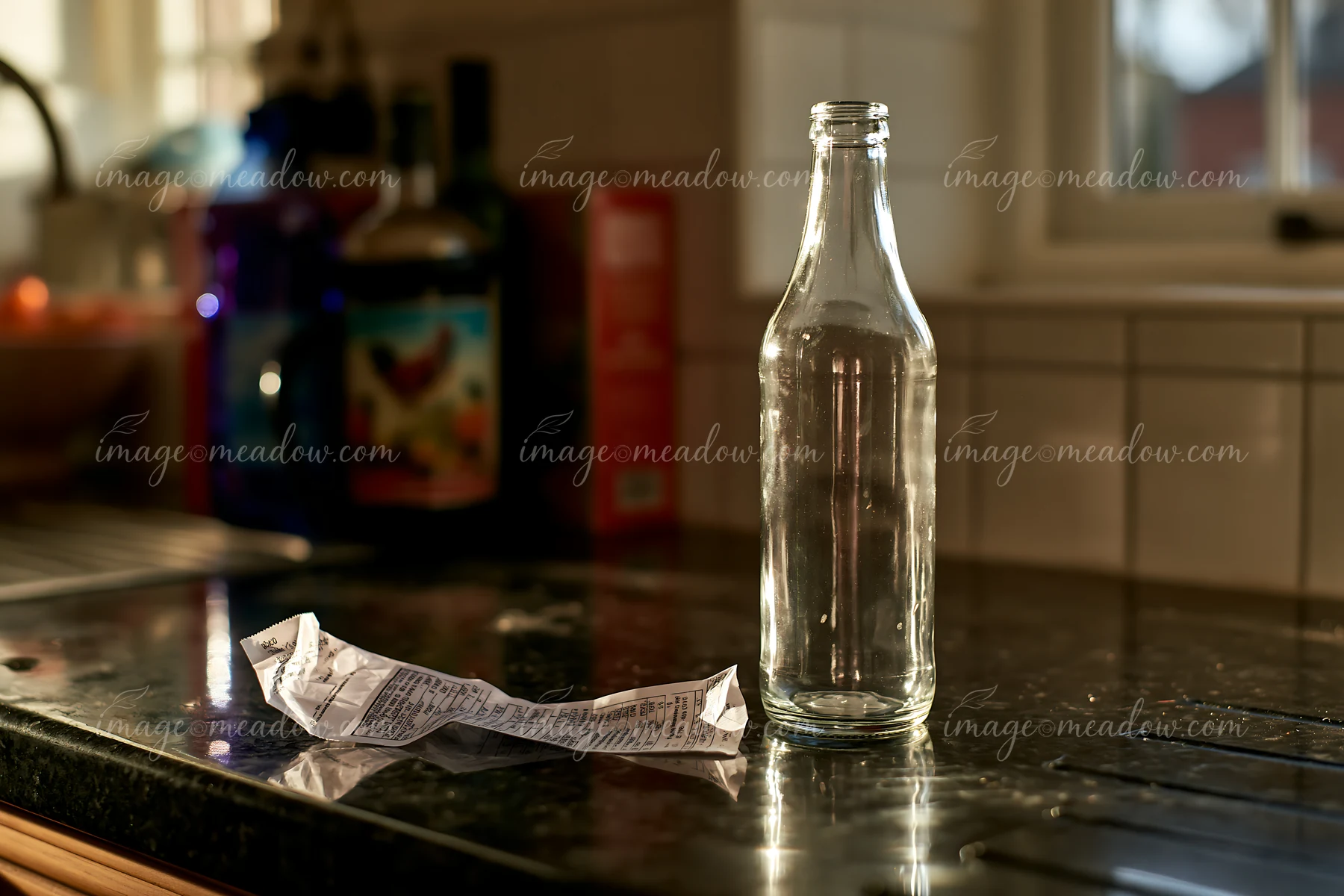 A clear glass bottle sits beside a crumpled receipt on a stone kitchen countertop.