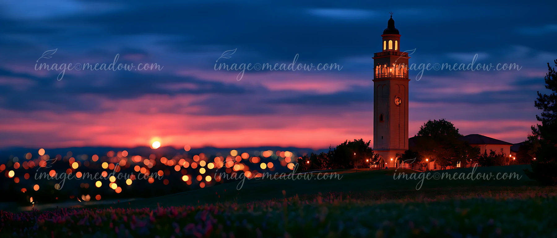 A clock tower stands against a vibrant sunset with city lights twinkling in the distance.