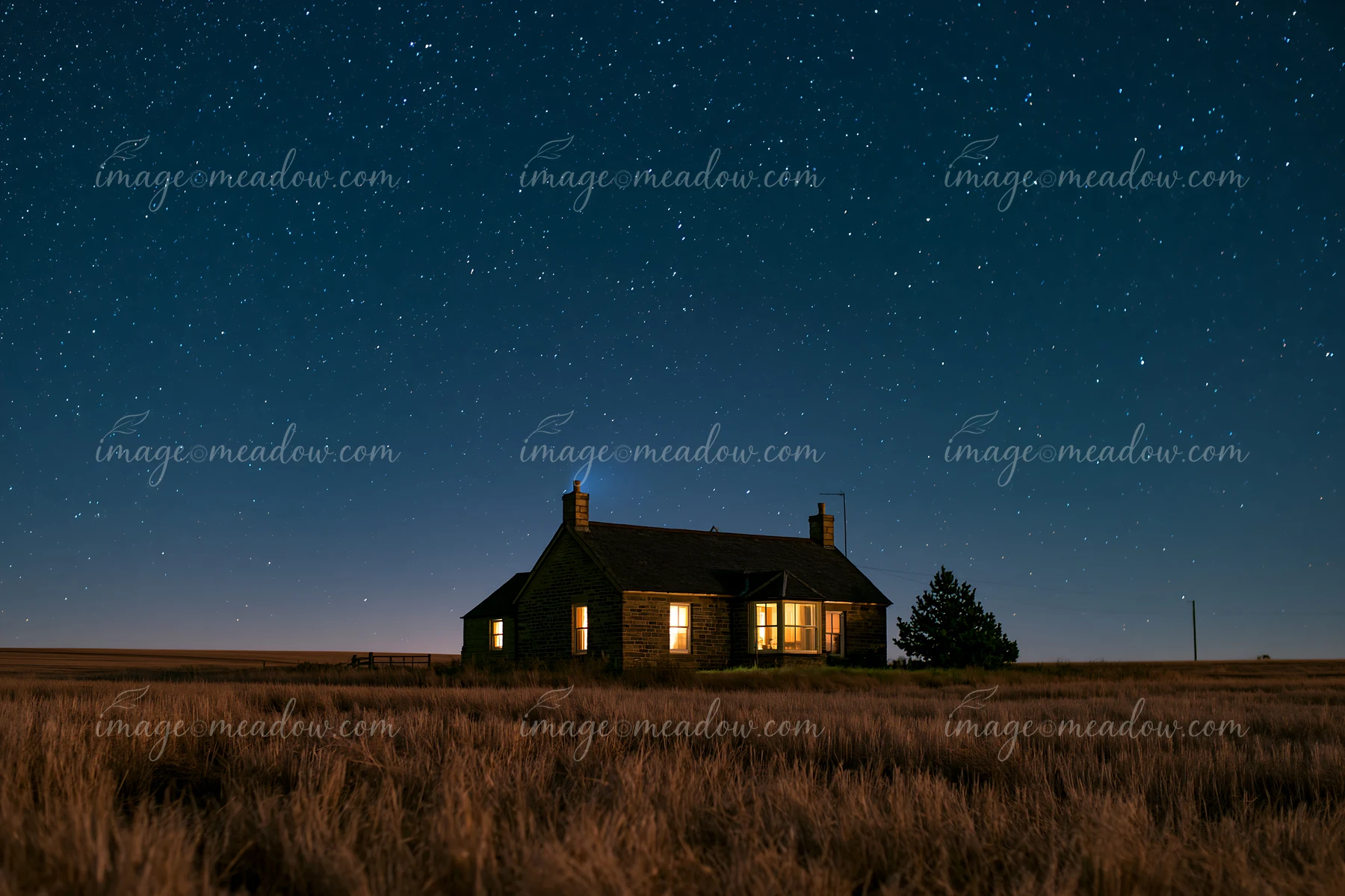 A country house stands alone in a field, illuminated by warm light from its windows.