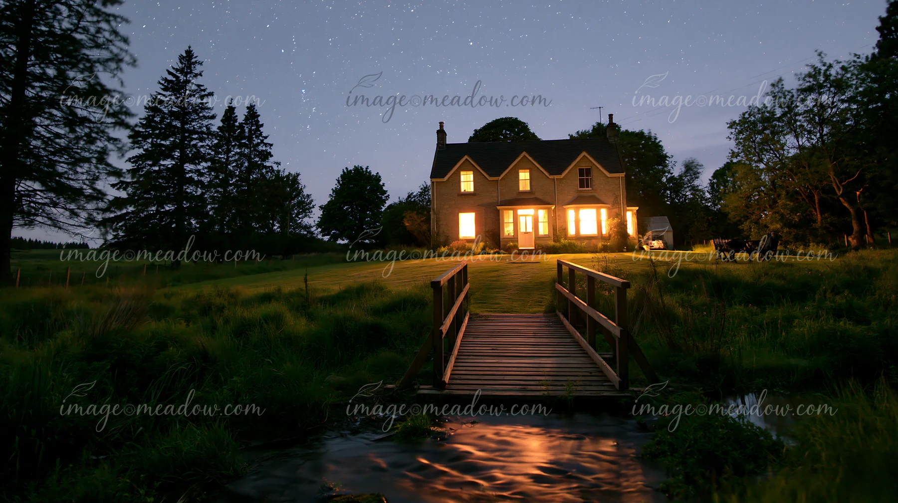 A country house stands under a starry sky with light shining from its windows.