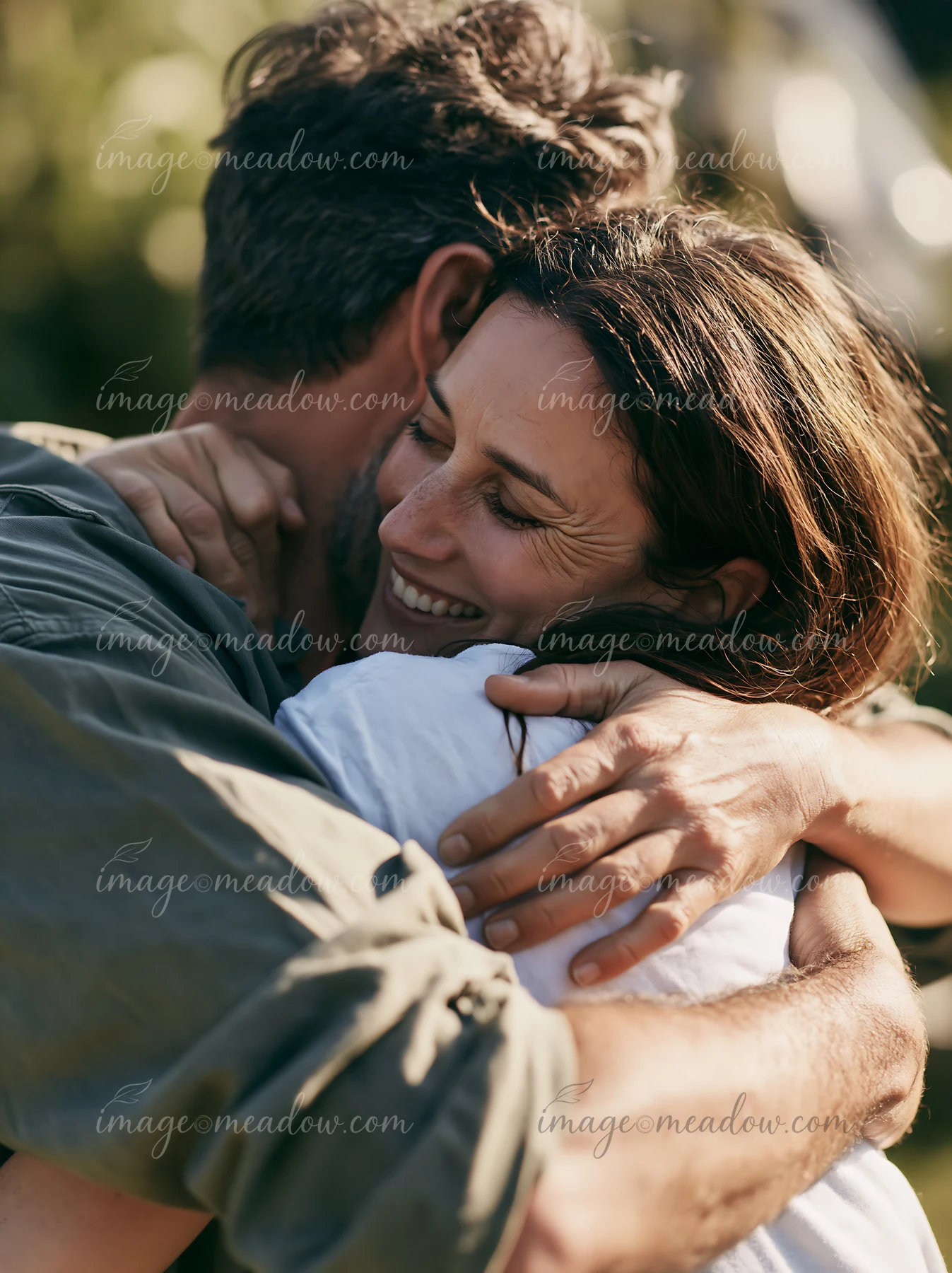 A couple embraces outdoors in spring with smiles, surrounded by green foliage.