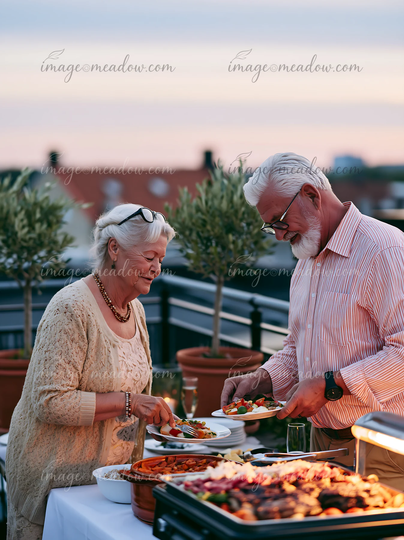 A couple enjoys a rooftop buffet dinner while serving themselves various dishes.