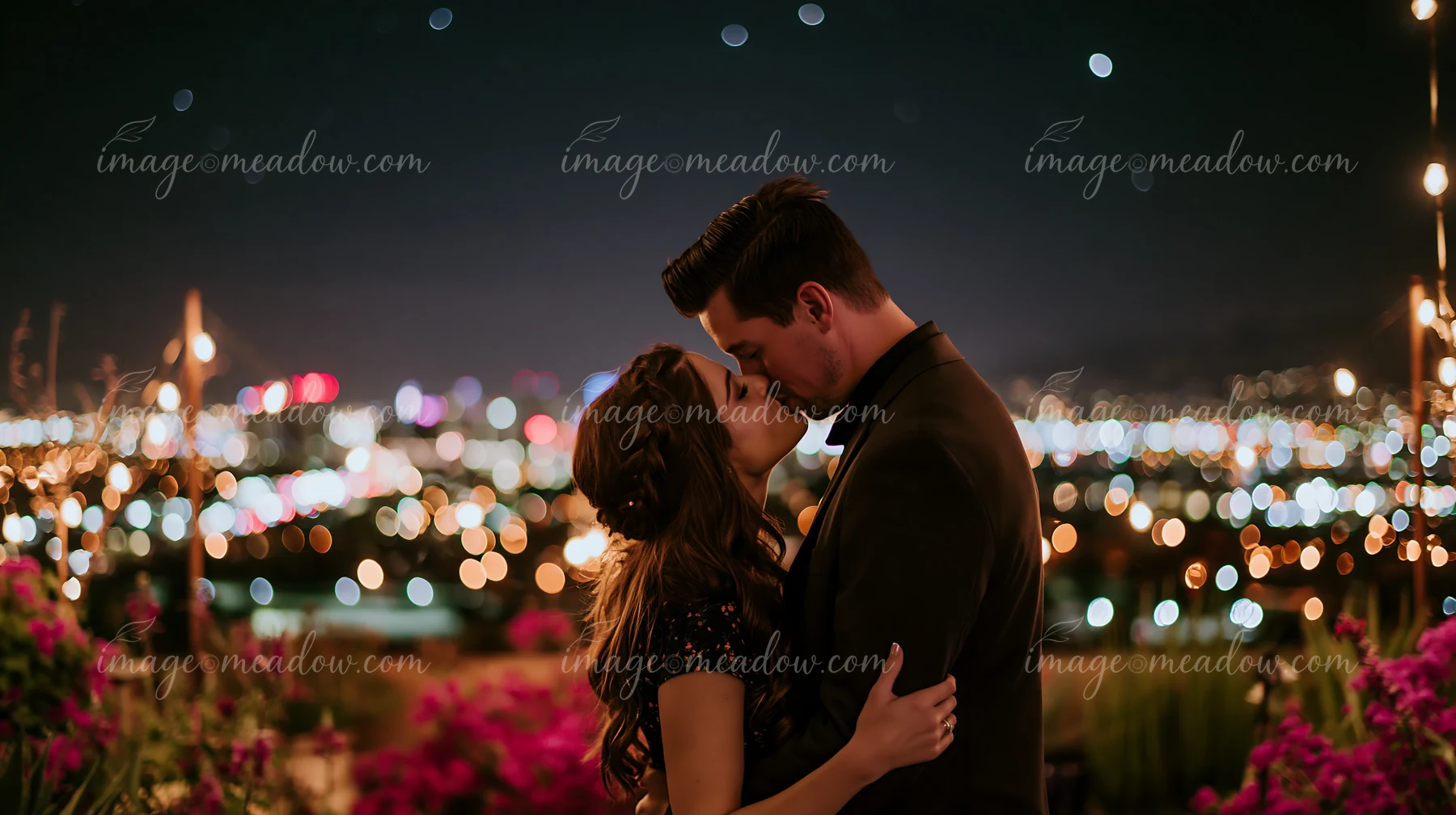 A couple leans in for a romantic anniversary kiss under stars with a city skyline in the background.