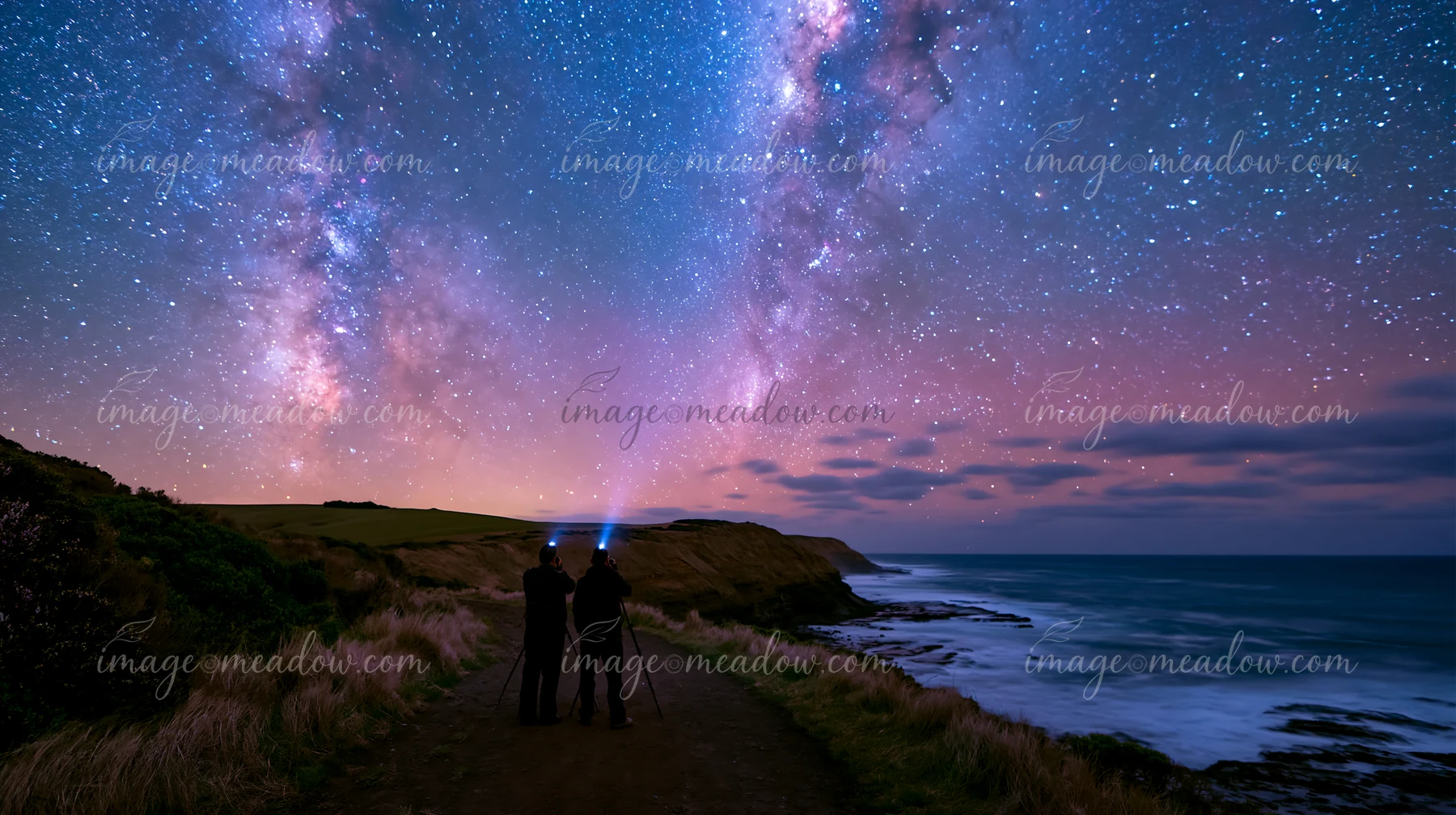 A couple photographing the Milky Way along the coastline under a starry sky.