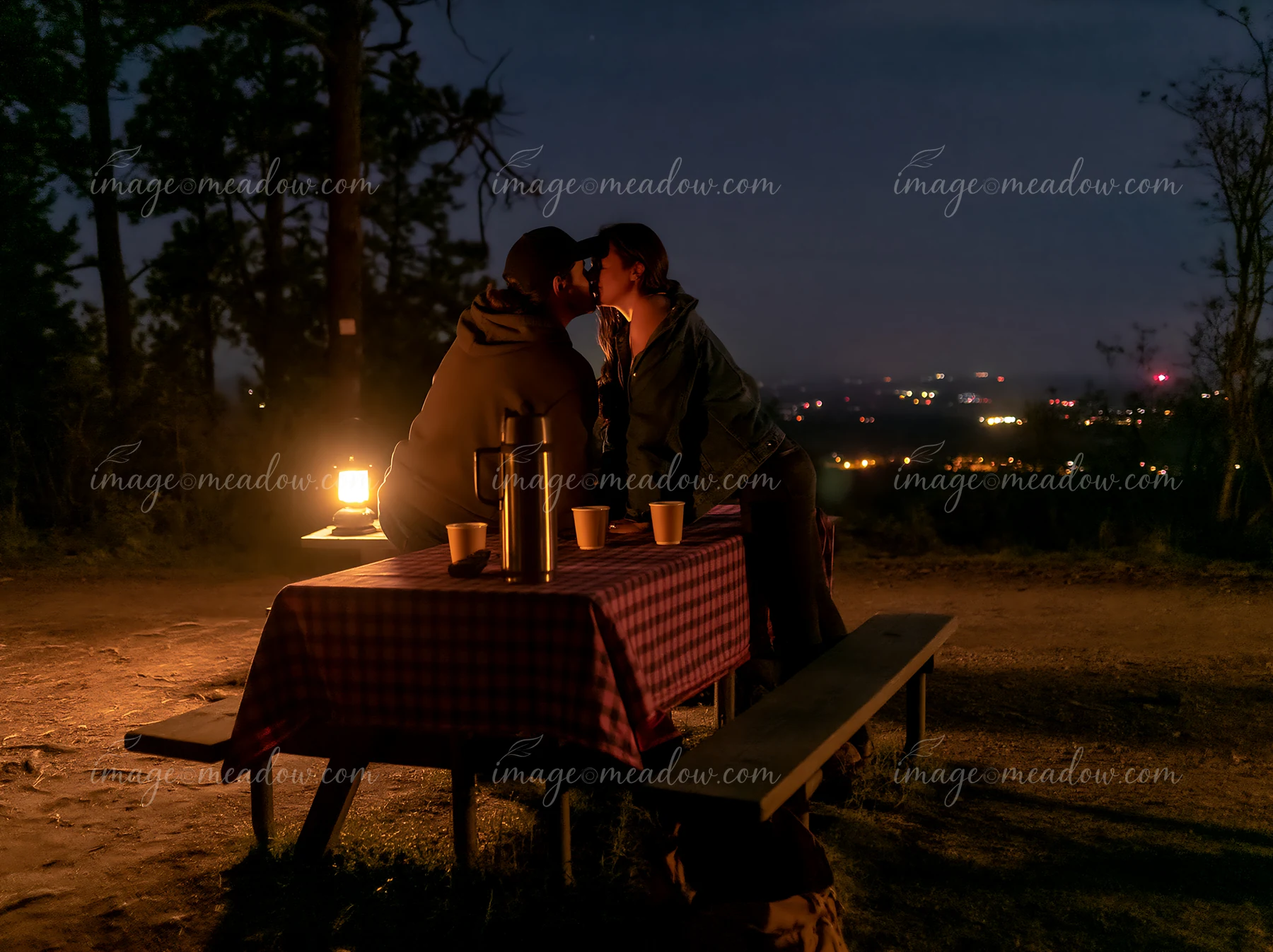 A couple shares a kiss on a mountain overlook while illuminated by a lantern.
