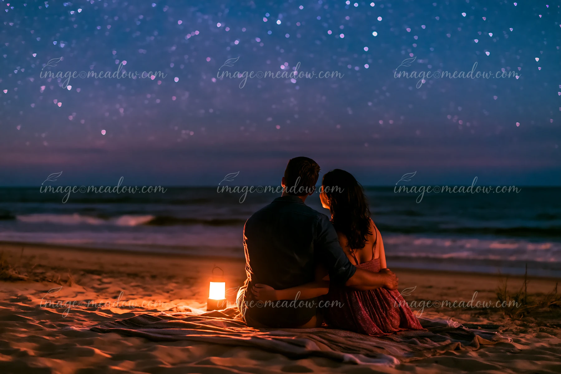 A couple sits closely together on a sandy beach under a starry night.