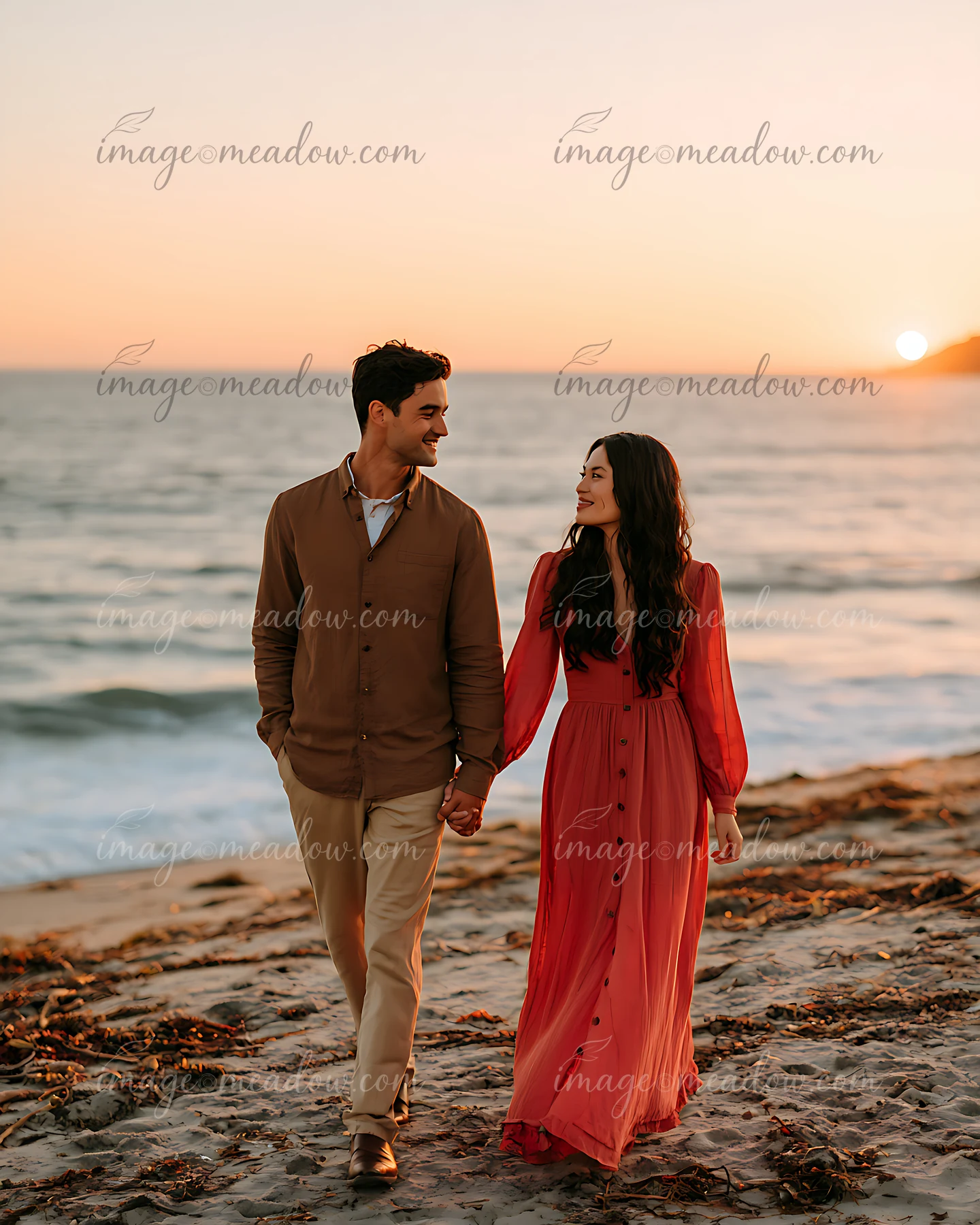 A couple walks hand in hand along the sandy beach as the sun sets over the ocean.