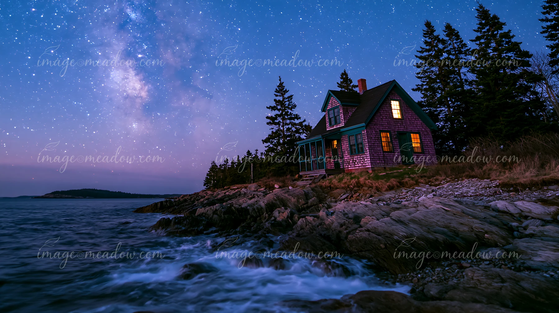 A cozy home sits by the shoreline as the Milky Way lights up the night sky.