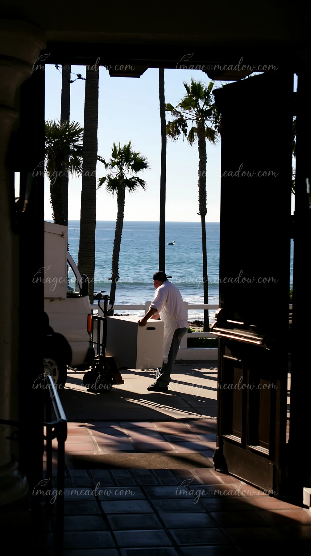 A delivery person pushes a cart with a wedding cake towards a venue near the ocean.