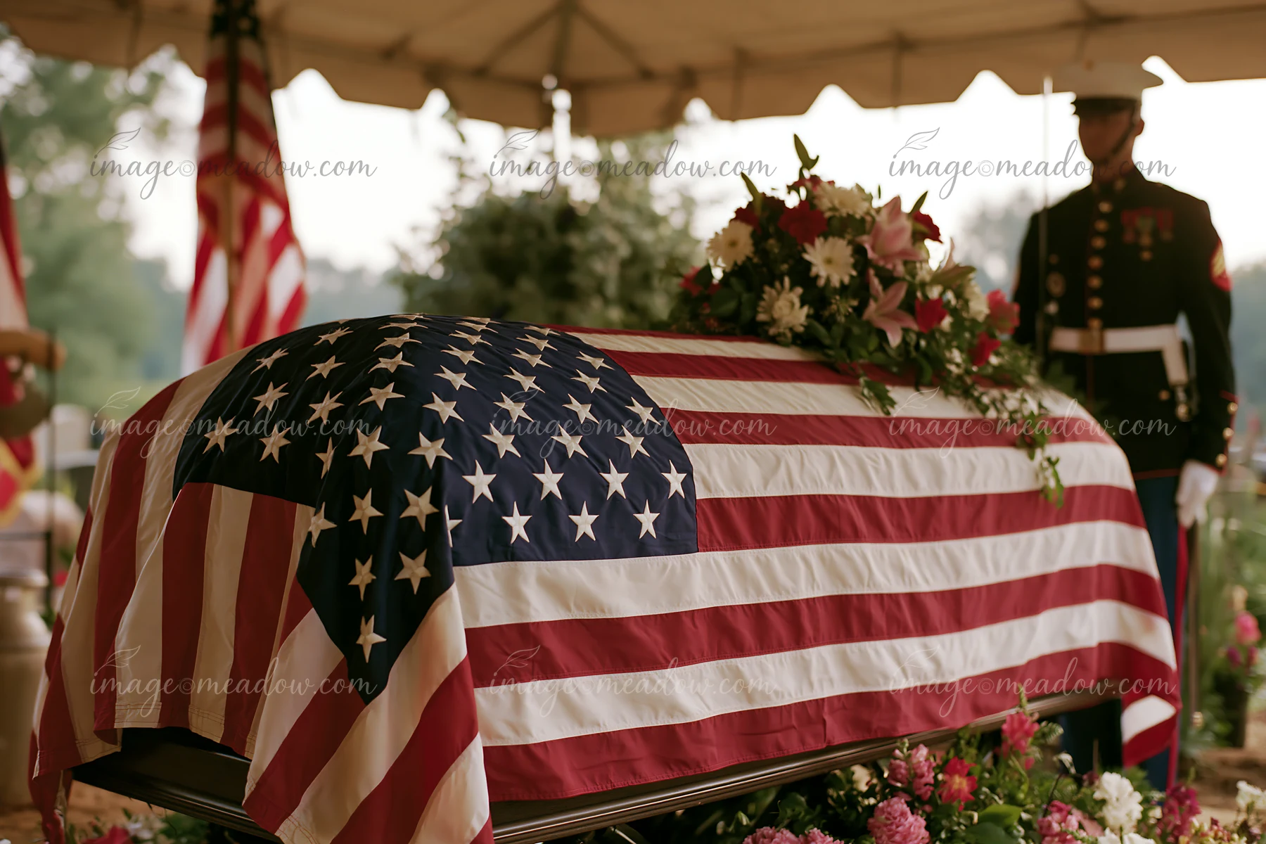 A flag-draped coffin during veteran funeral service stands under a tent surrounded by flowers.