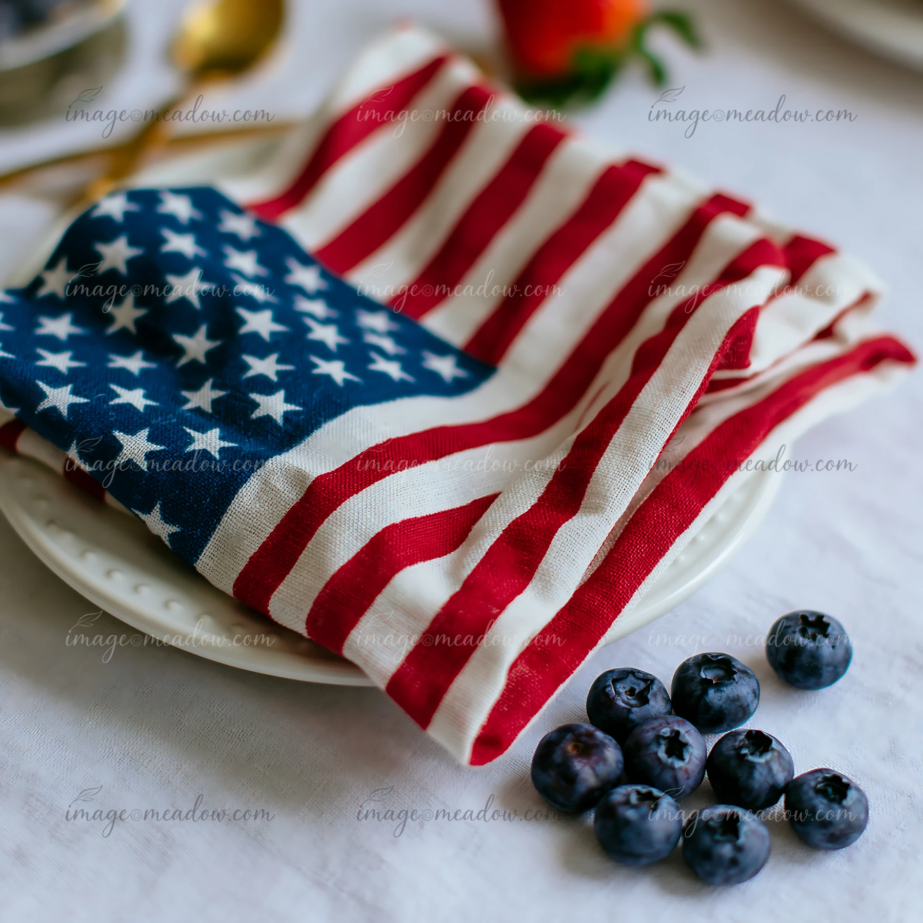 A folded American flag table decoration rests on a white plate next to fresh blueberries.