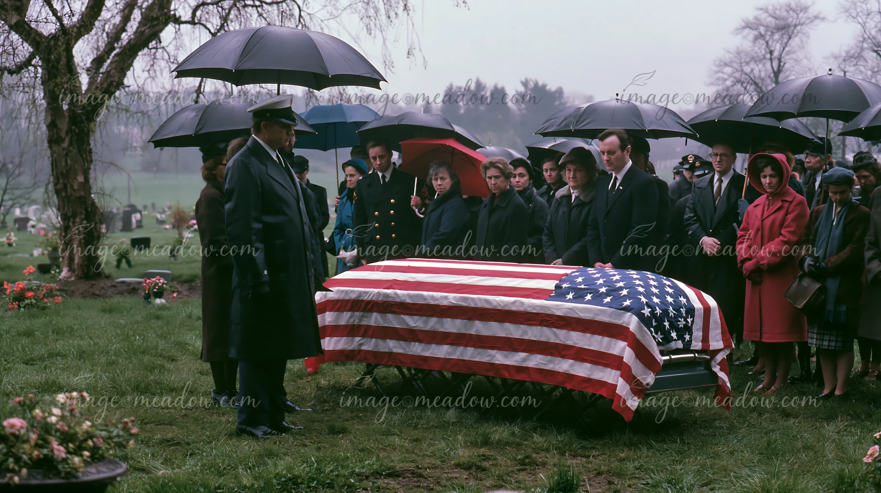 A group of mourners stands in a cemetery under umbrellas while attending a veteran's funeral.