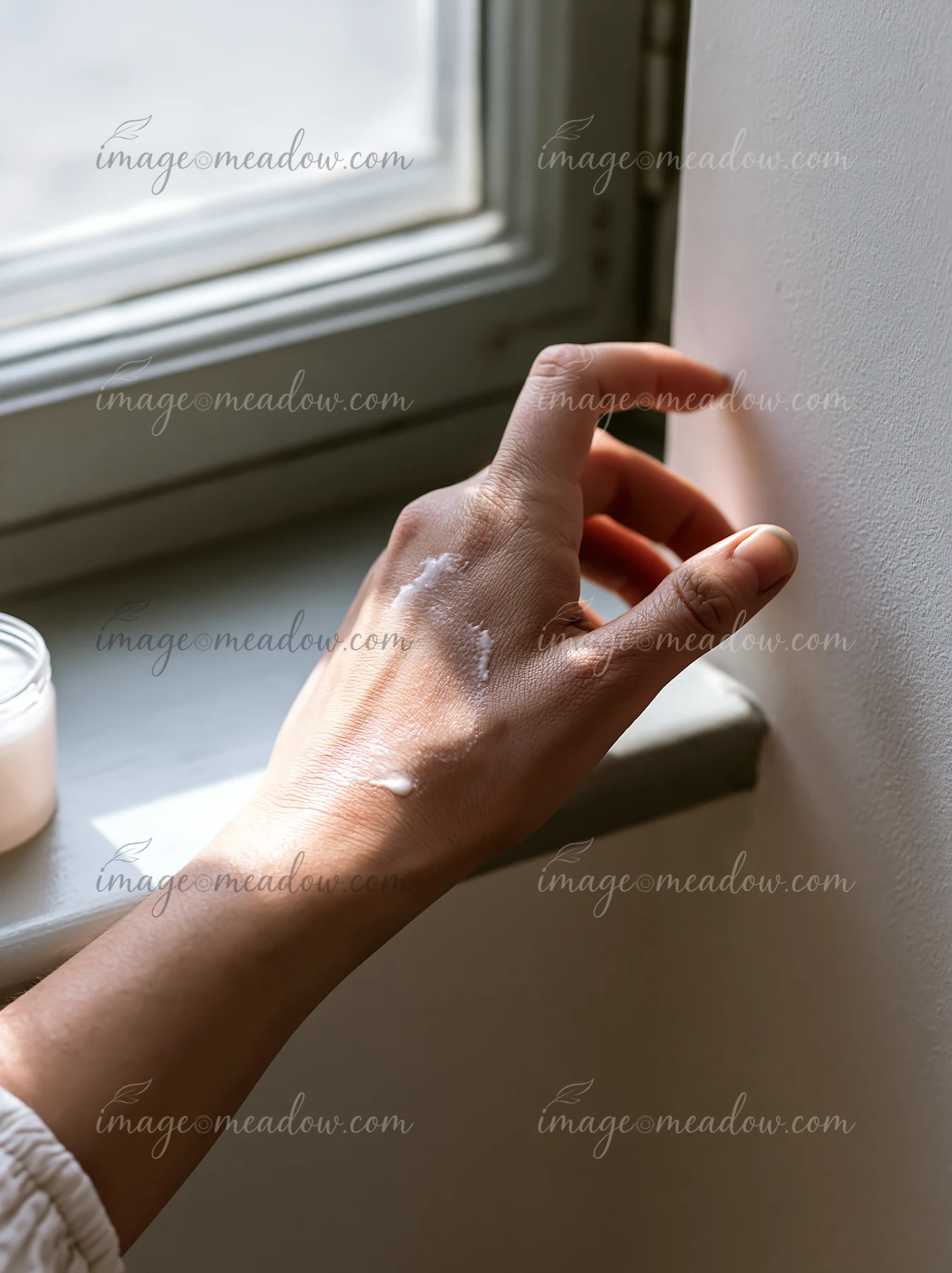 A hand reaches towards a wall with a small amount of cream visible.