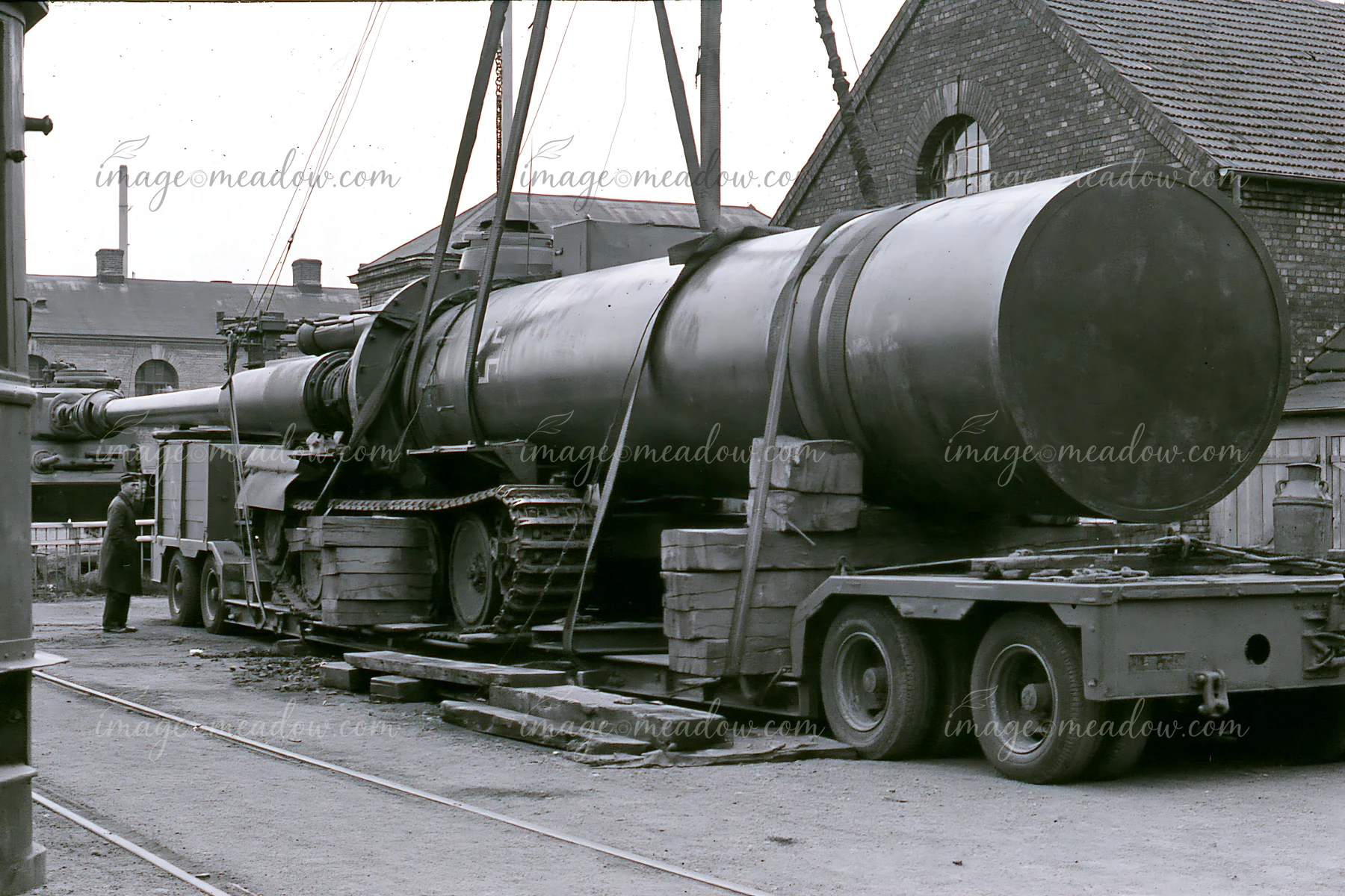 A large piece of artillery is being loaded onto a transport vehicle at a railway yard.