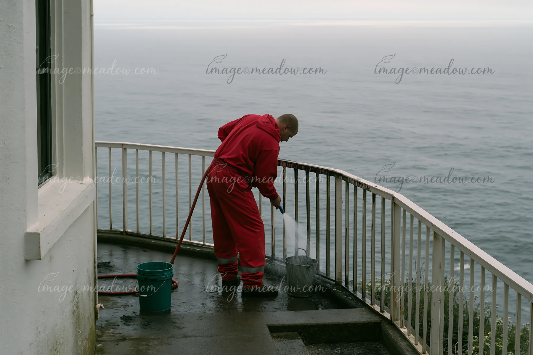 A lighthouse maintenance worker at work cleans the railing and surrounding area near the water.