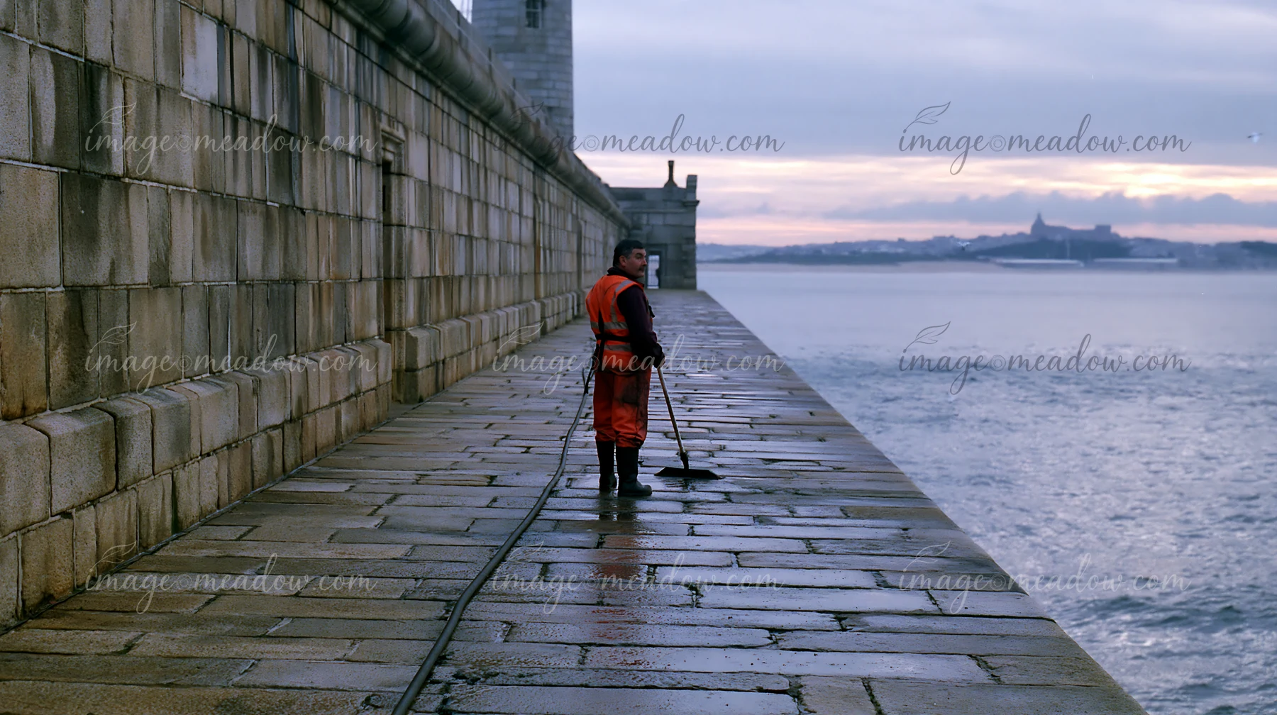 A lighthouse maintenance worker at work cleans the stone walkway along the sea.