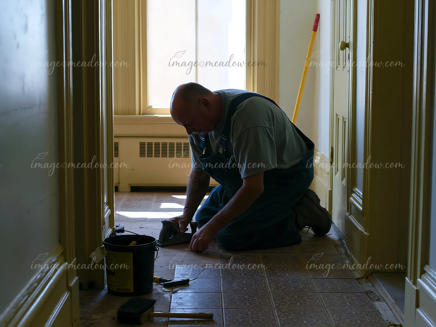 A lighthouse maintenance worker at work kneels on the floor while applying materials.