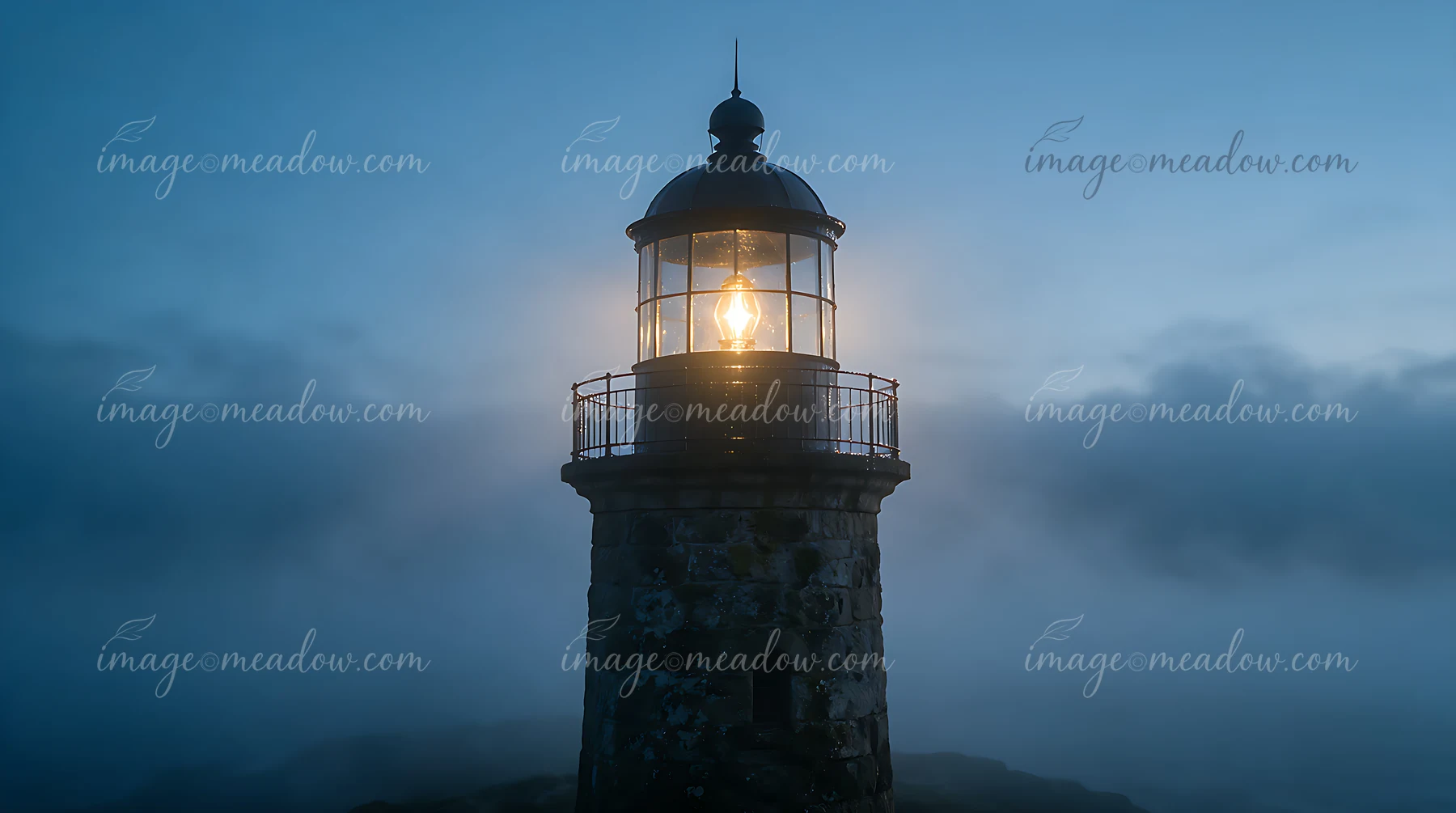A lighthouse stands tall in heavy ocean fog with its light shining brightly.