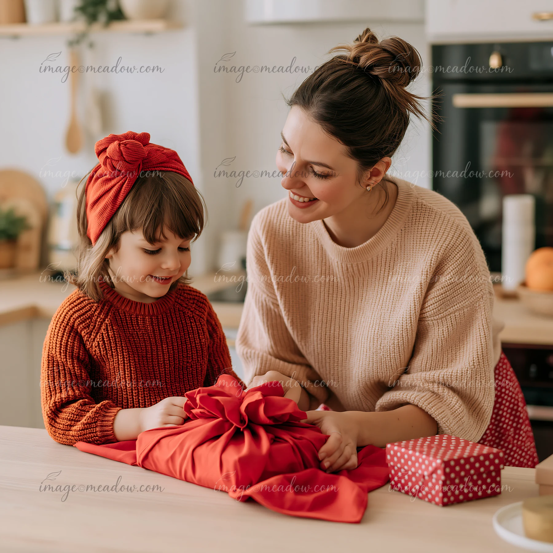 A mother helps her daughter with gift wrapping on a kitchen table.