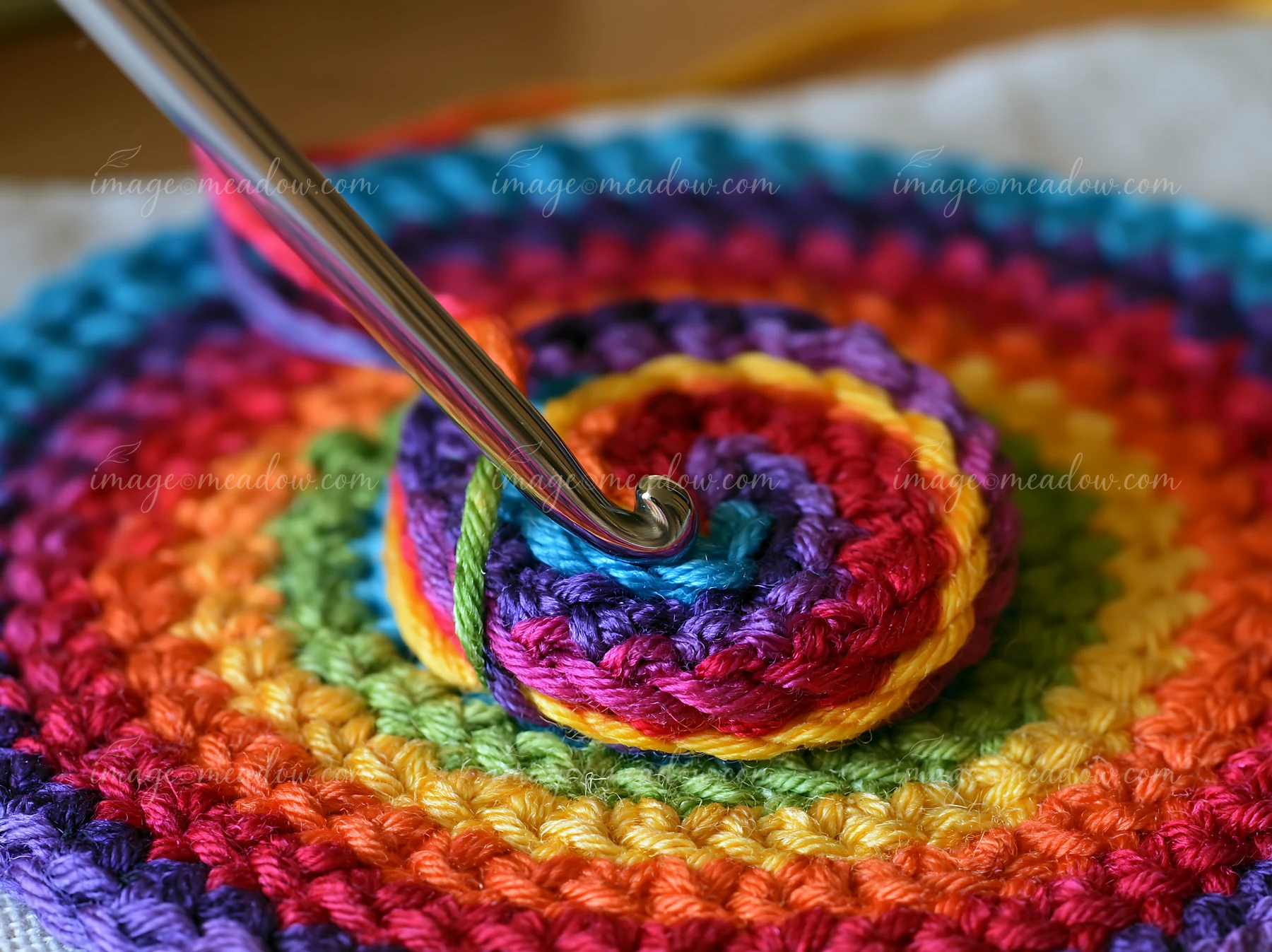 A person holds a crochet hook while winding rainbow thread in a spiral.
