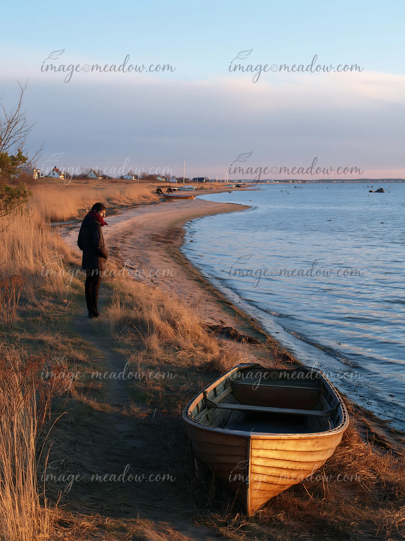 A person stands on a sandy coastline, looking at the water with a small boat nearby.