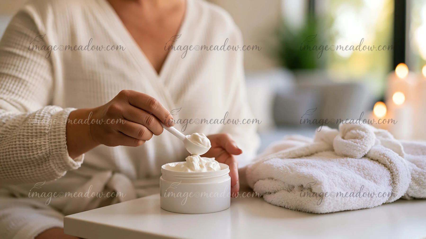 A person uses a cosmetic scoop to measure out cream from a container at a bathroom counter.
