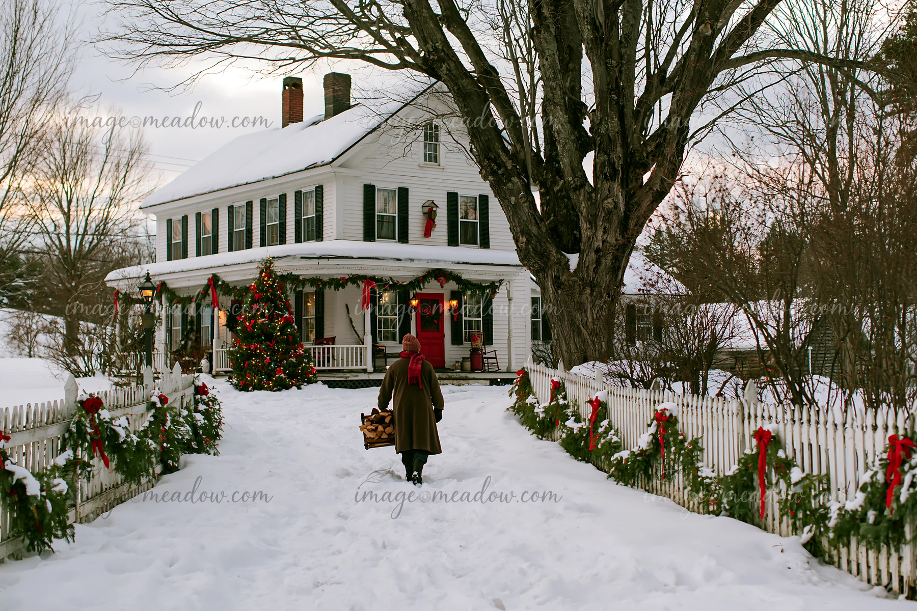 A person walks toward a snowy country house adorned with Christmas decorations.