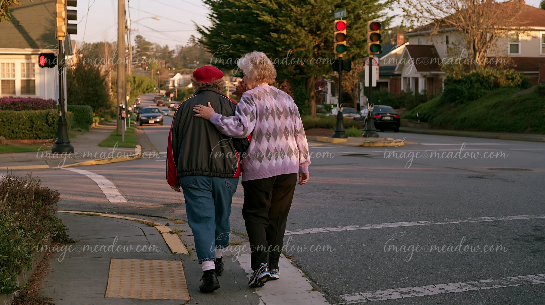 A person with Parkinson's disease receiving support walks along the street in a residential area.