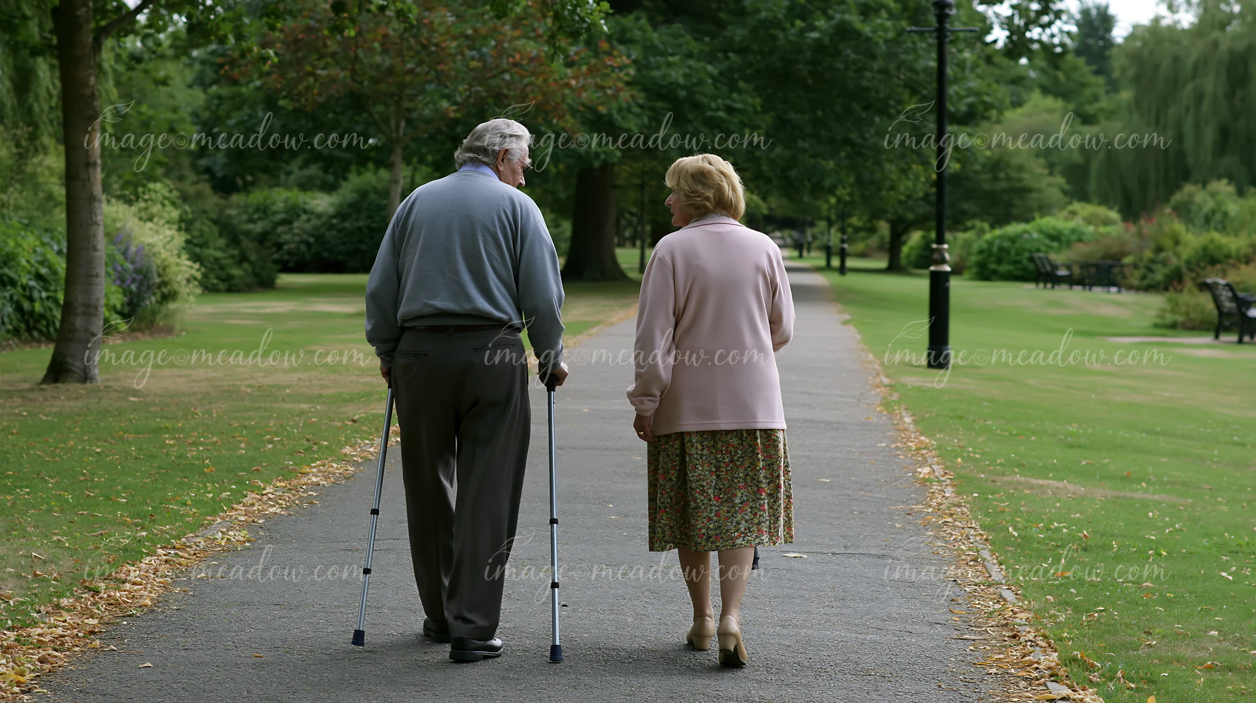 A person with Parkinson's disease receiving support walks with a companion in a green park.