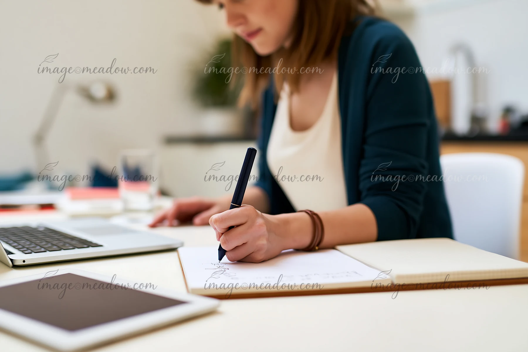 A person writes a gift list on paper while seated at a desk.