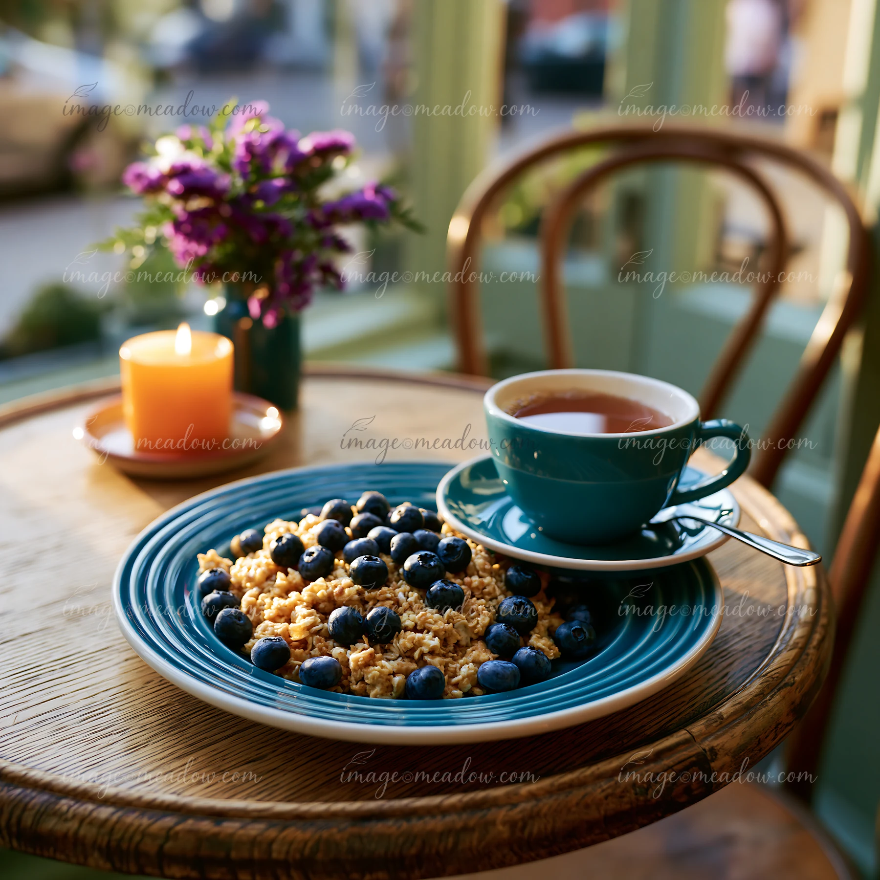 A plate with blueberries and granola sits on a wooden table next to a cup of tea.