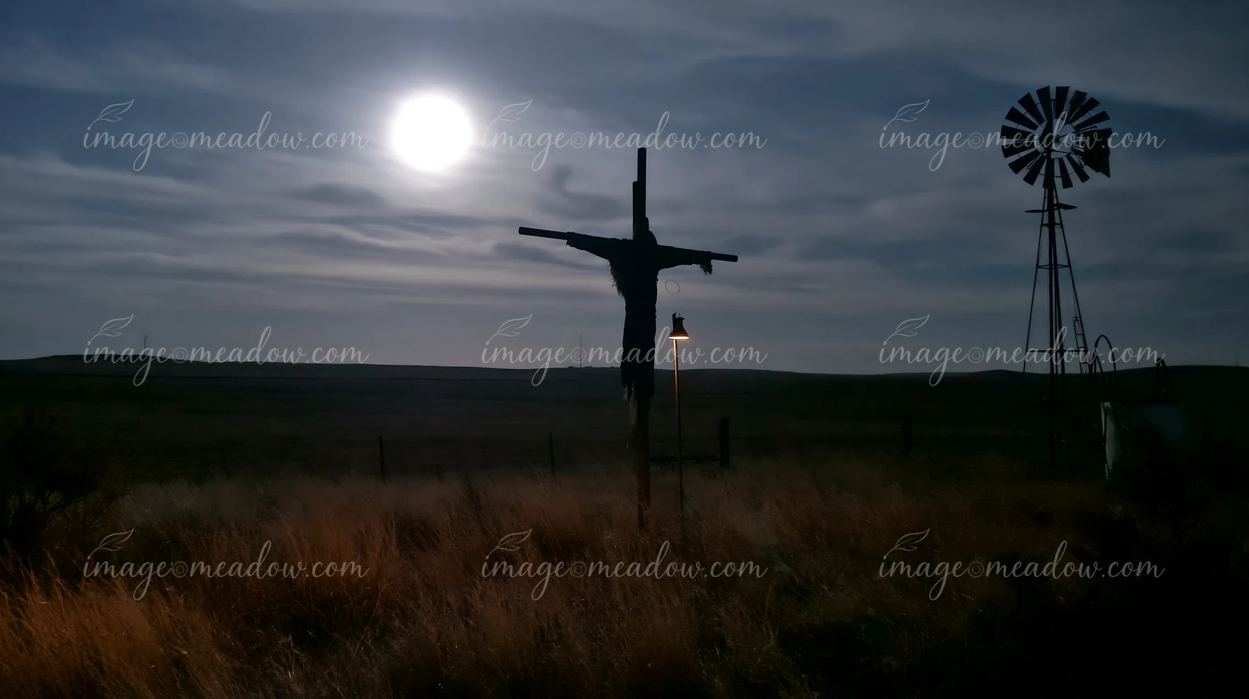 A scarecrow in a moonlit field holds its position against the night sky, while a windmill stands quietly nearby.