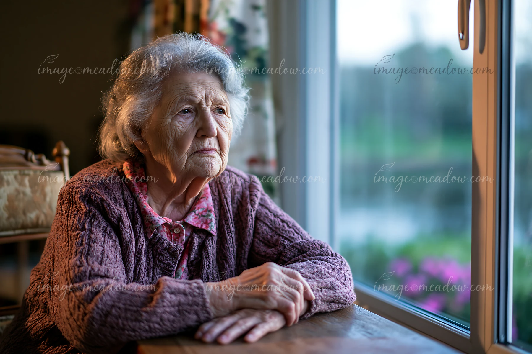 A senior with Alzheimer's looking out a window while seated at a table.