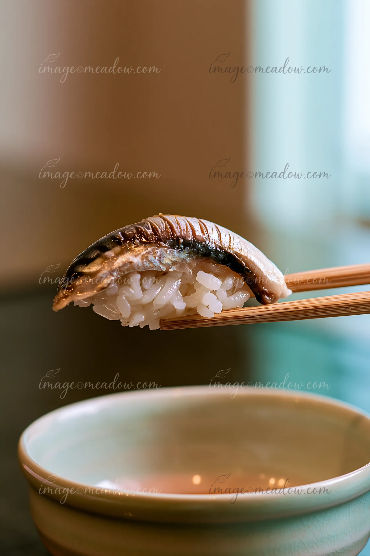 A single sushi piece ready to eat with chopsticks is held above a small bowl.