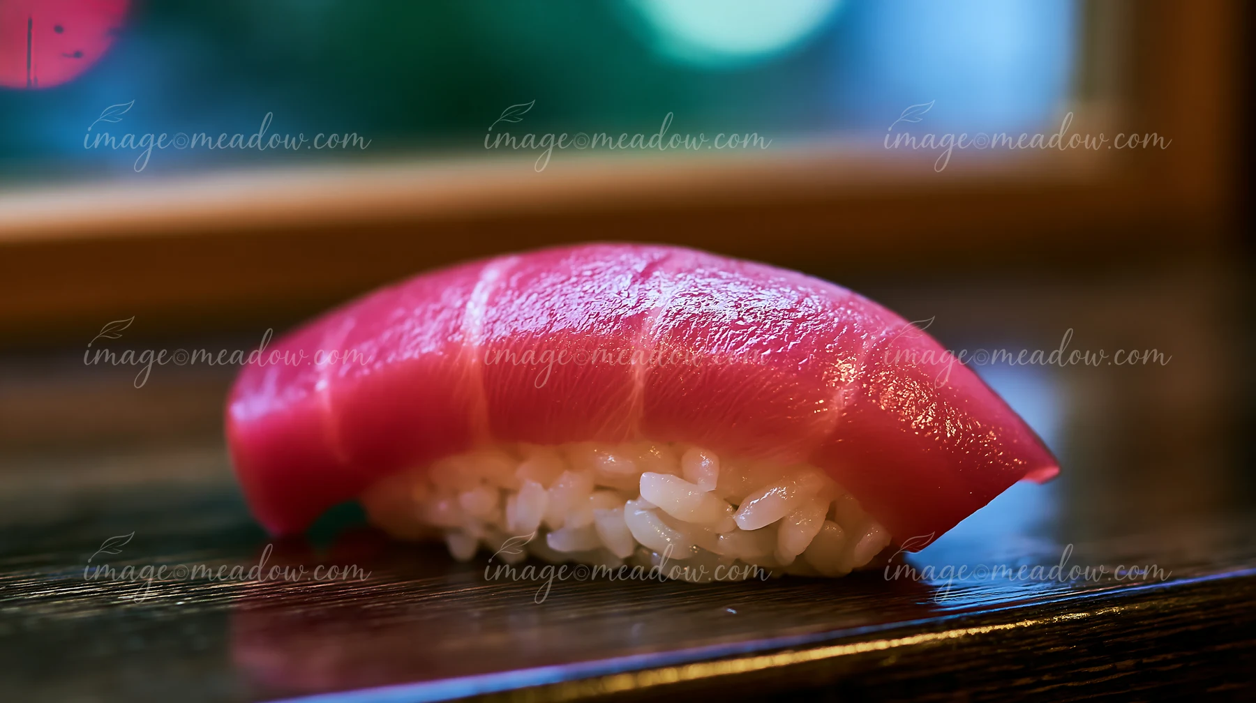 A single sushi piece with colorful fish topping rests on a wooden table.