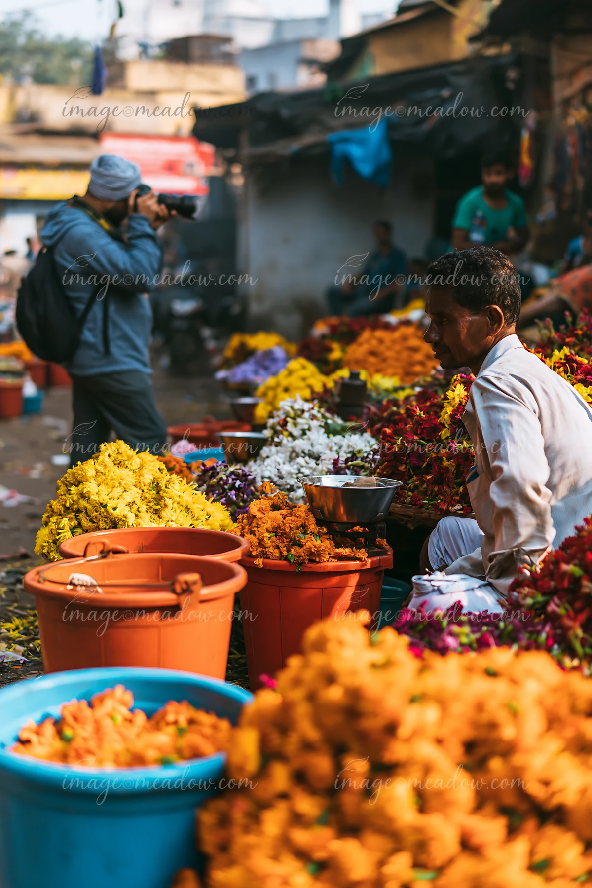 A street photographer taking pictures in an urban market filled with vibrant flower stalls.