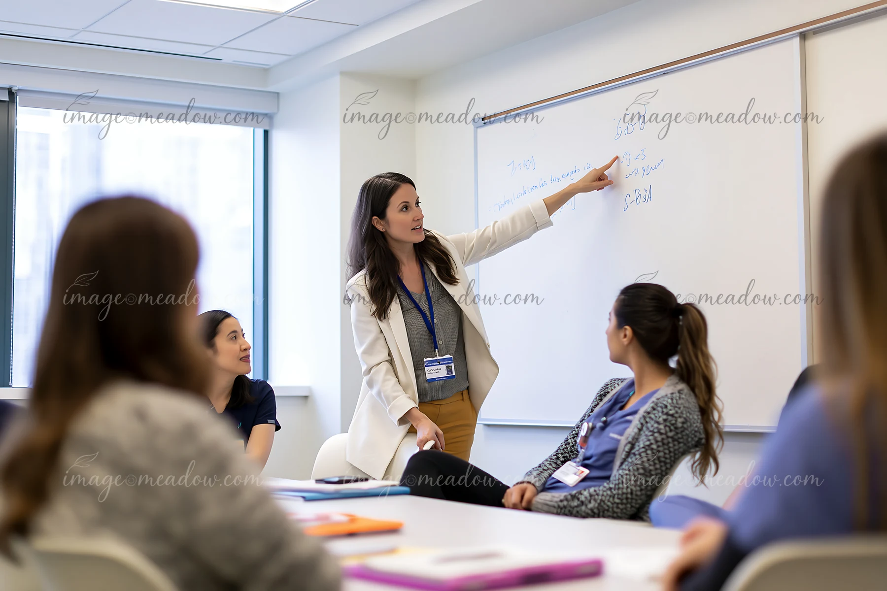 A team leader is pointing at a whiteboard while discussing ideas with her colleagues in a modern office setting.
