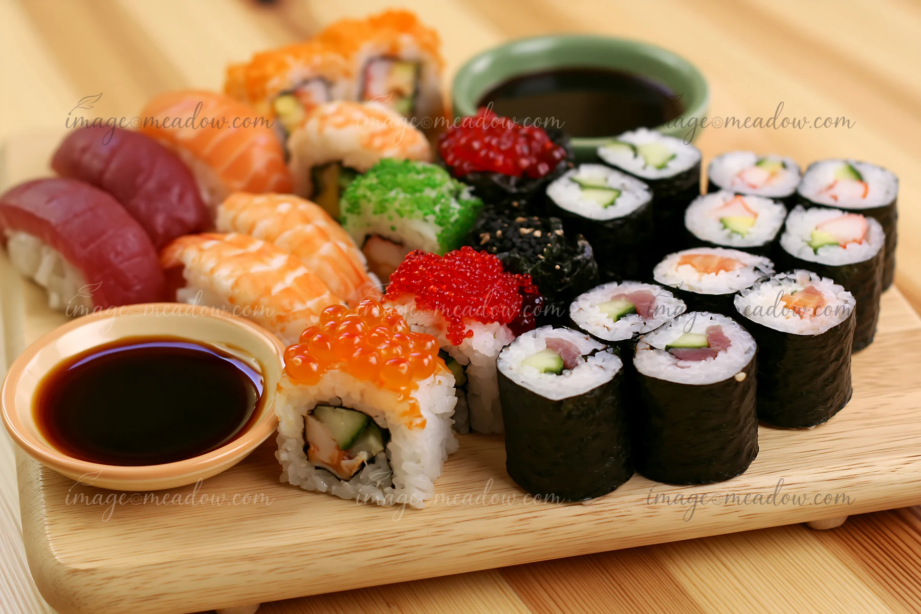 A variety of sushi types are displayed on a wooden platter, featuring colorful rolls and sauces.