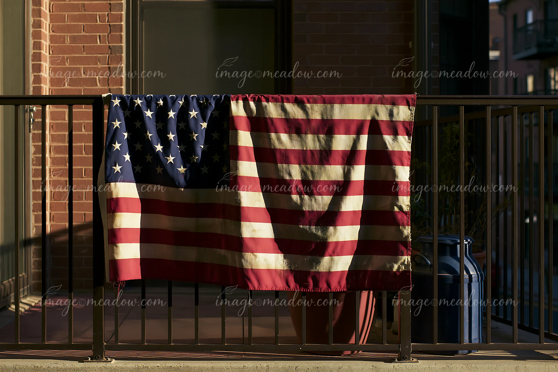 A weathered American flag drapes over a balcony railing, showing signs of fading and wear.