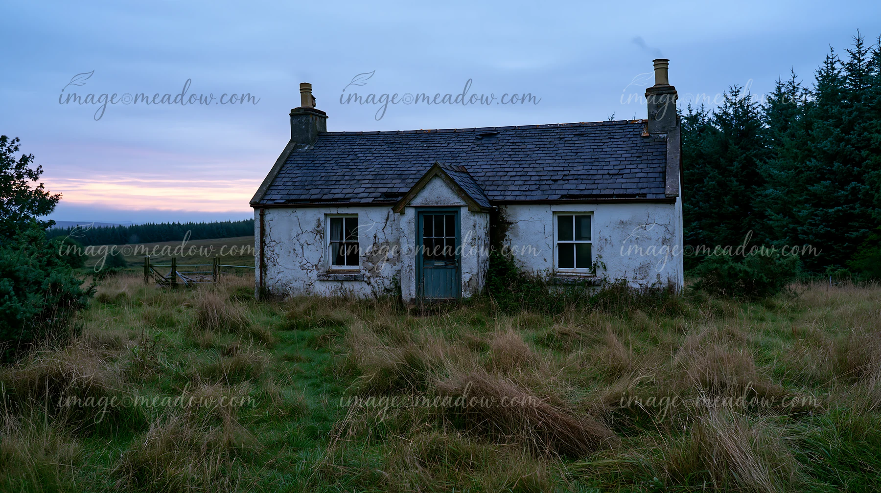 A weathered cottage stands alone in a grassy field surrounded by trees, with a cloudy sky above.