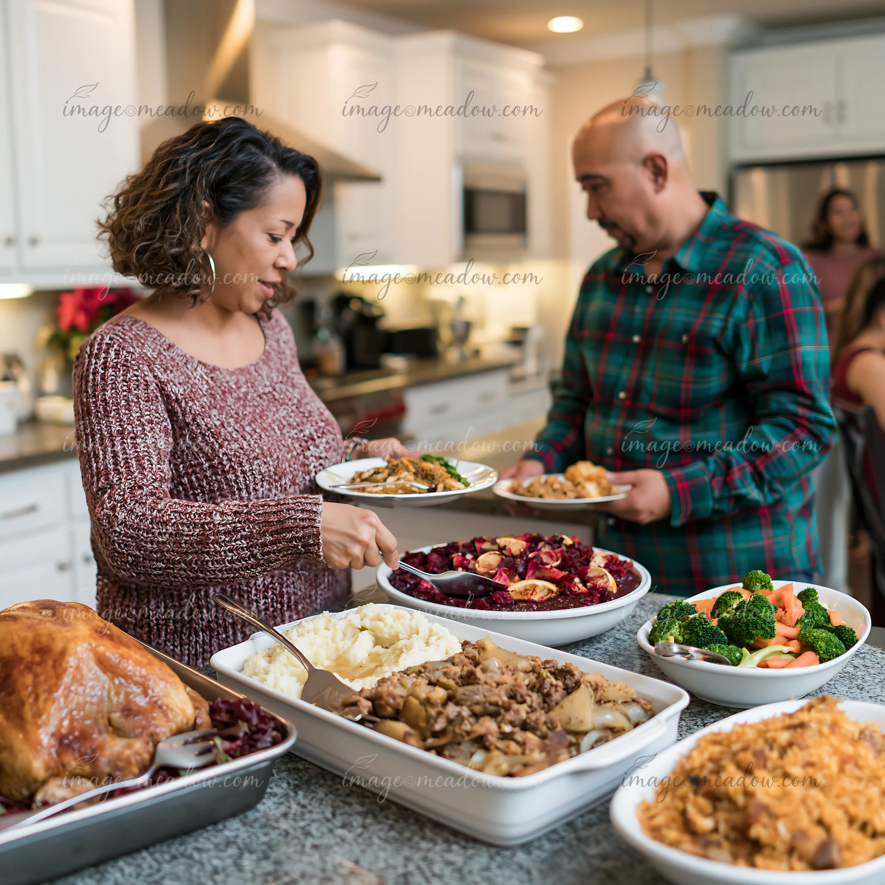 A woman and a man are serving food from large dishes onto their plates in a cozy kitchen.