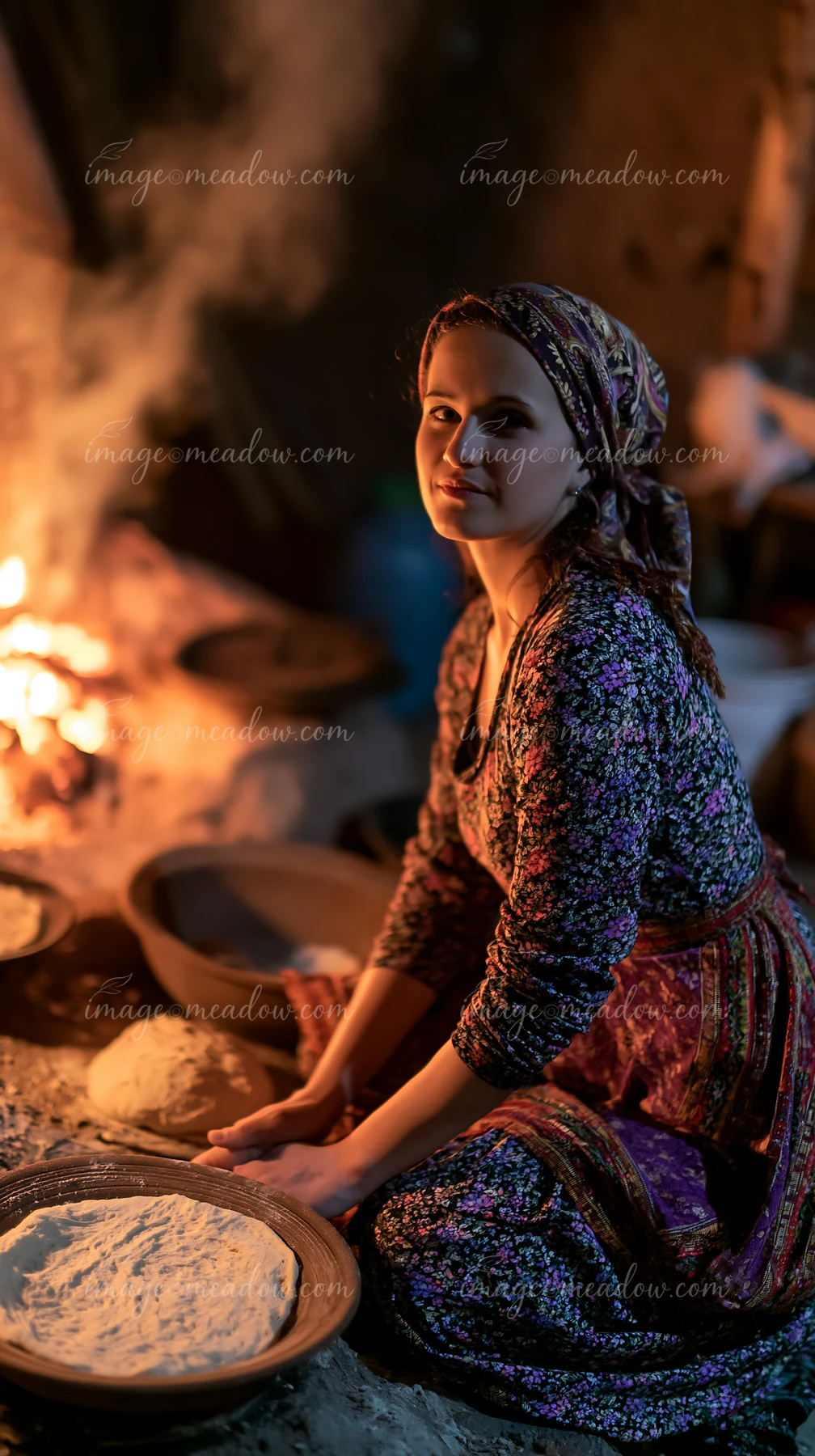 A woman in traditional dress prepares homemade bread in a rustic kitchen.