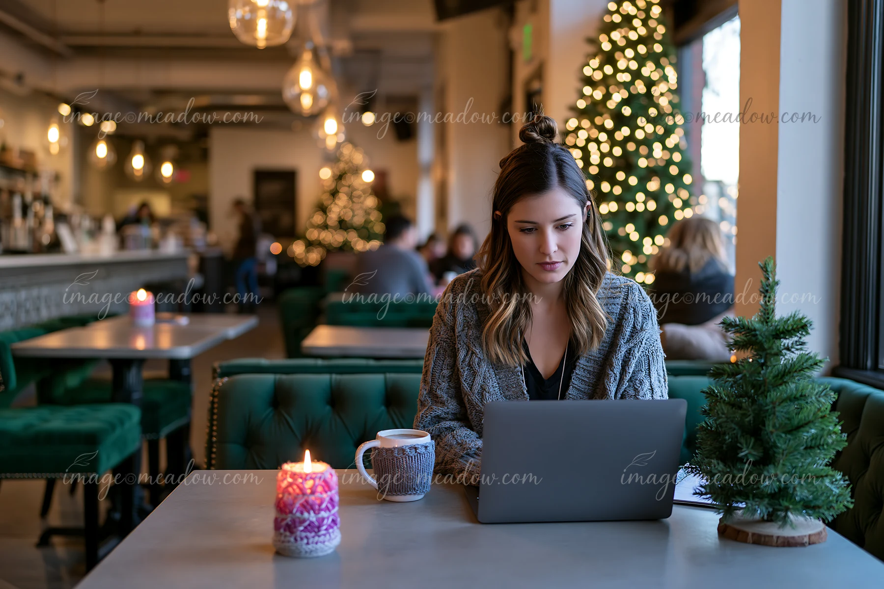 A woman works on a laptop at a table in a festive coffee shop.