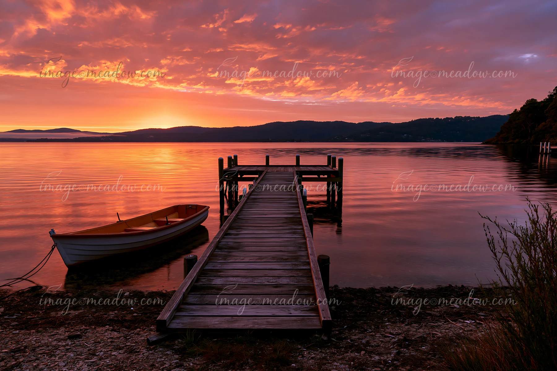 A wooden dock extends into calm waters at sunset, with a small boat resting nearby.