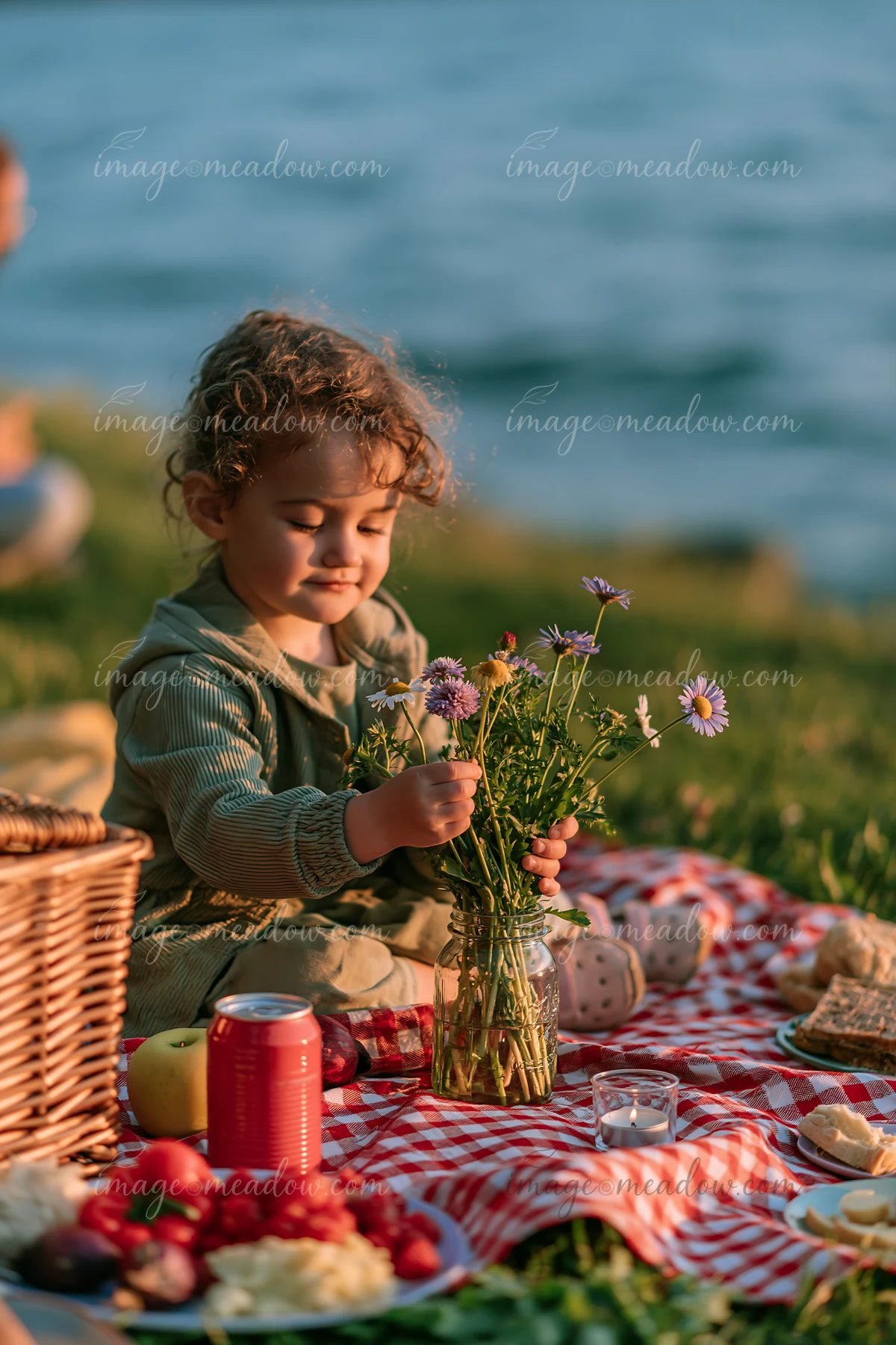 A young child enjoys a picnic by an alpine lake, arranging wildflowers in a vase.