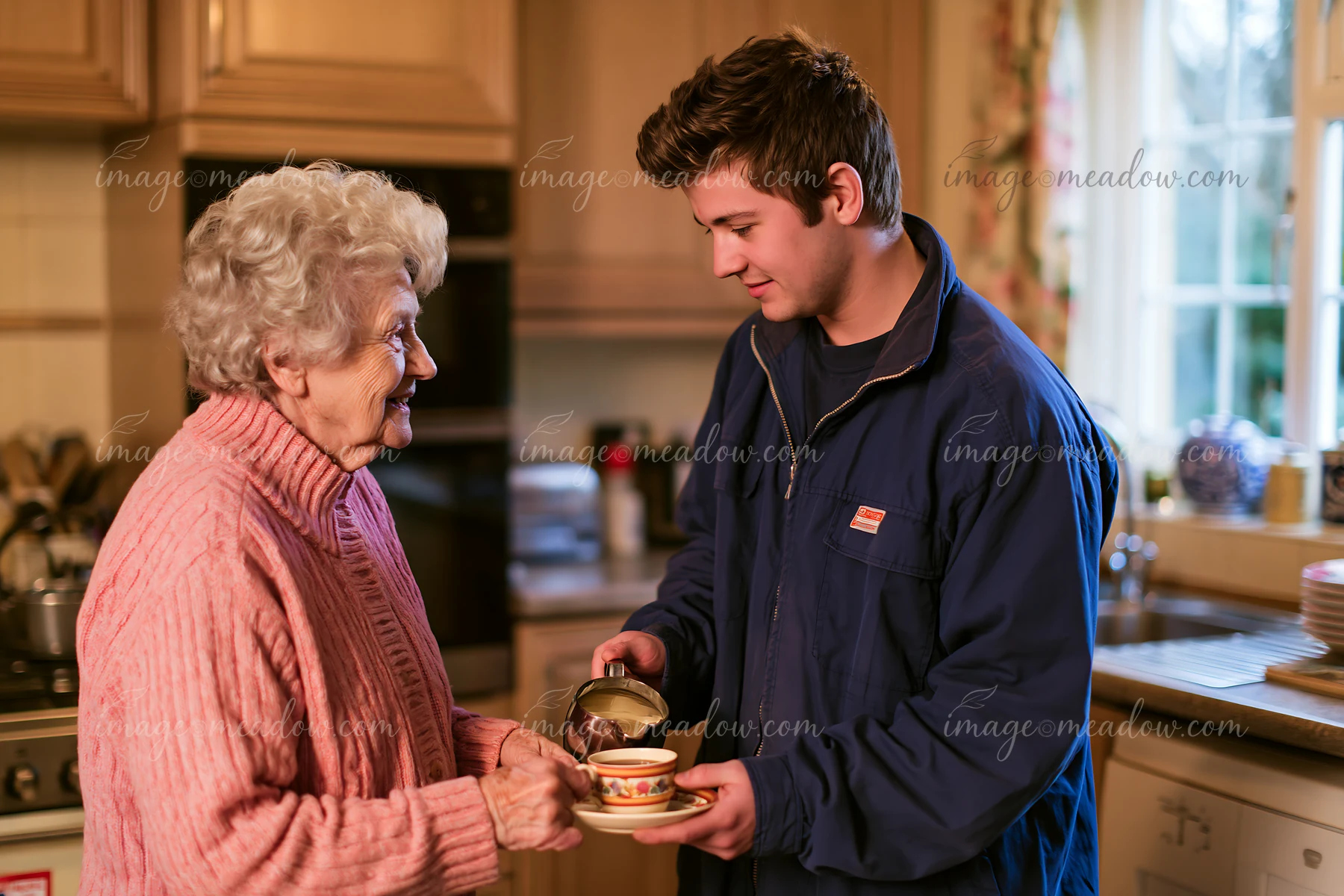 A young man serves tea to an older woman in a cozy kitchen setting.